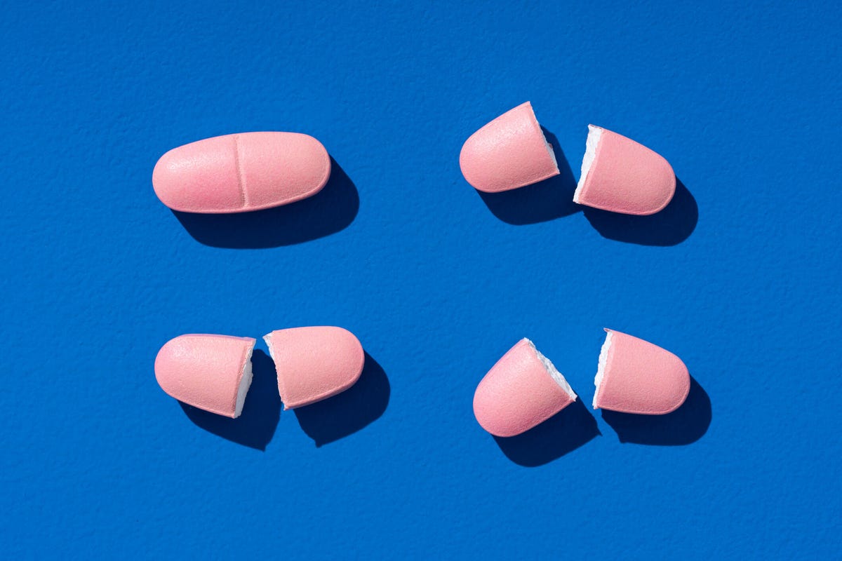 Pink vitamin supplements cut in half over a royal blue background.