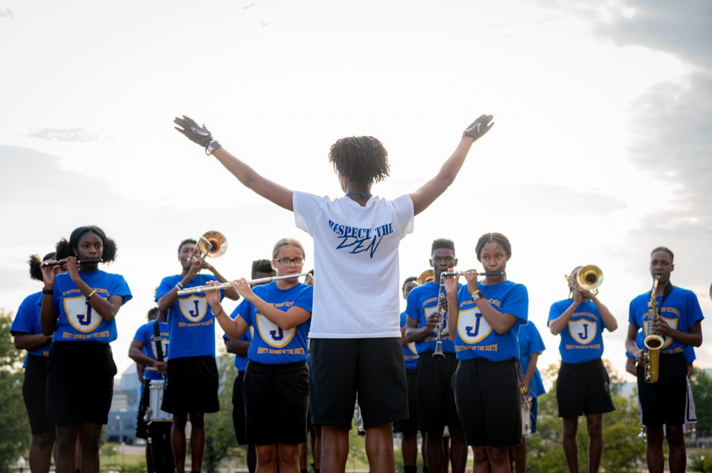 The drum major for the Mae C. Jemison High School Band lifts her arms to direct the band outside City Hall on Sept.  22, 2022. She is wearing a white T-shirt that says 